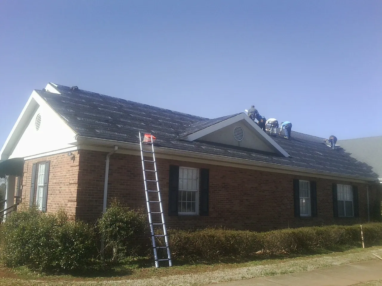 Crew tearing shingles off a brick ranch roof with a ladder set — Metal Roof Repair work by our crew in Elora