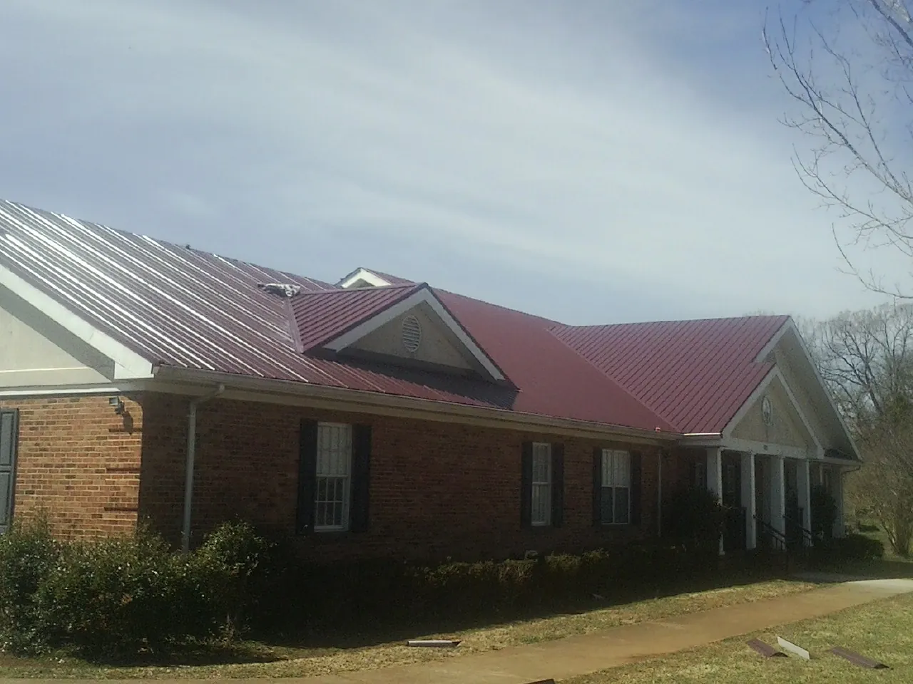 Red metal roof with gabled entries on a long brick building, from a Hail Damage Roof Repair job in Elora