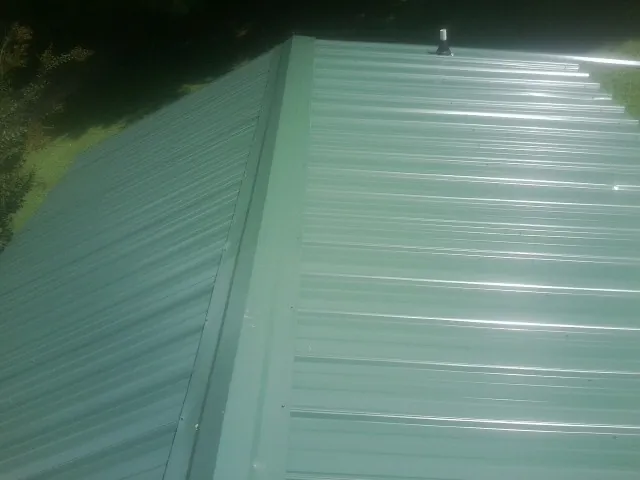 New green metal panels meeting at the ridge of a roof — Flat Roof Repair work by our crew in Elora