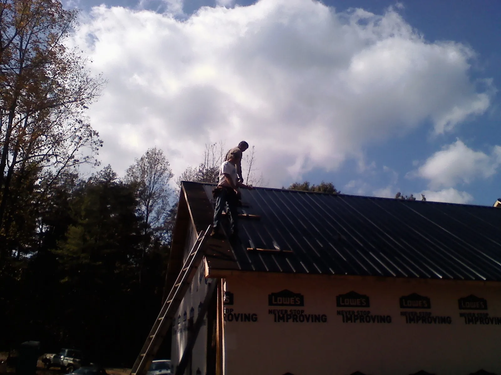 Roofer fastening dark metal panels high against a cloudy sky, from a Roof Inspection job in Elora
