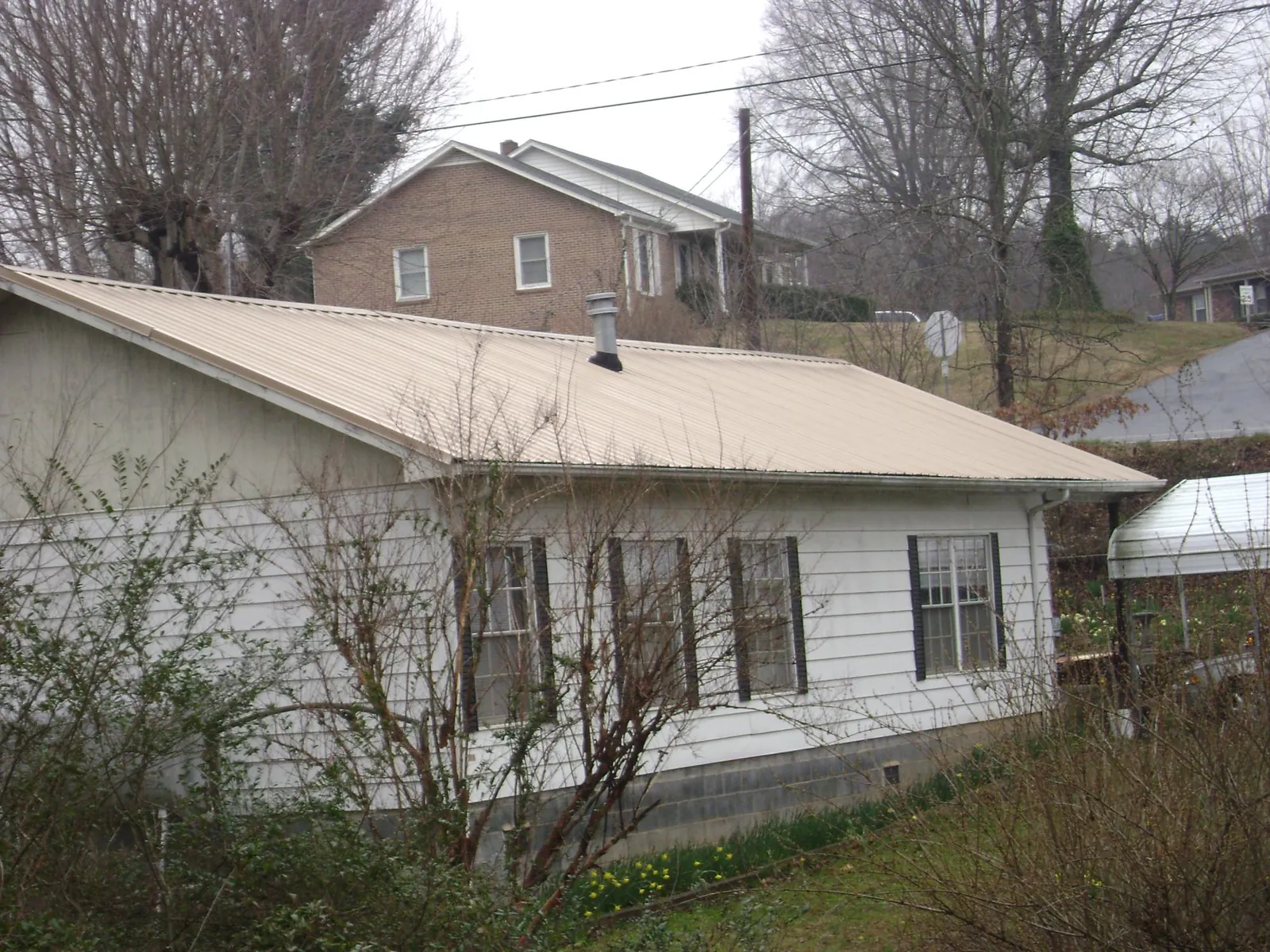 Tan metal roof on a white sided house set into a hillside — Commercial Roofing by Roofing Brothers in Elora